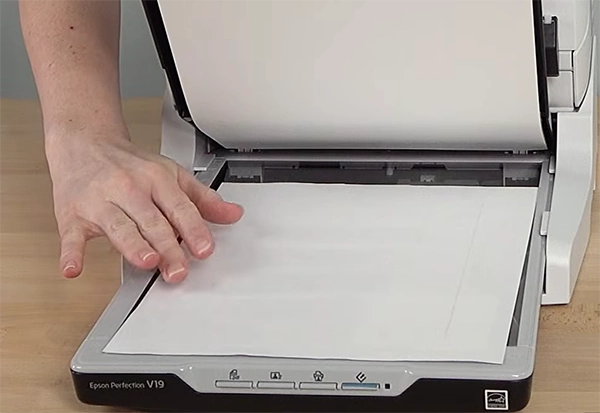 a persons hand keeping a paper in the flatbed scanner
